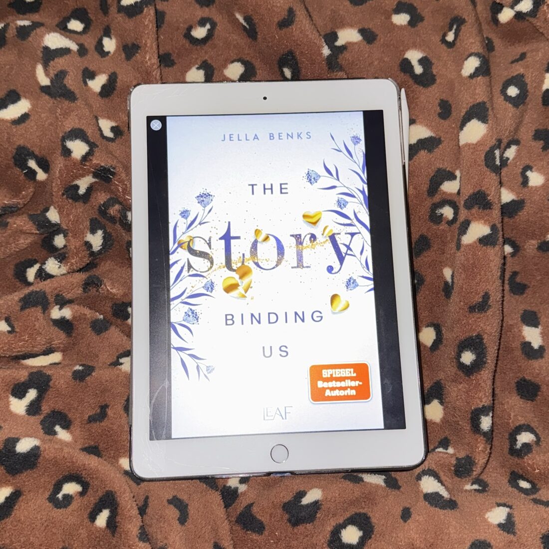 E-Book mit dem Titel 'The Story Binding Us' auf einem Tablet, umgeben von einem gepunkteten Stoff.