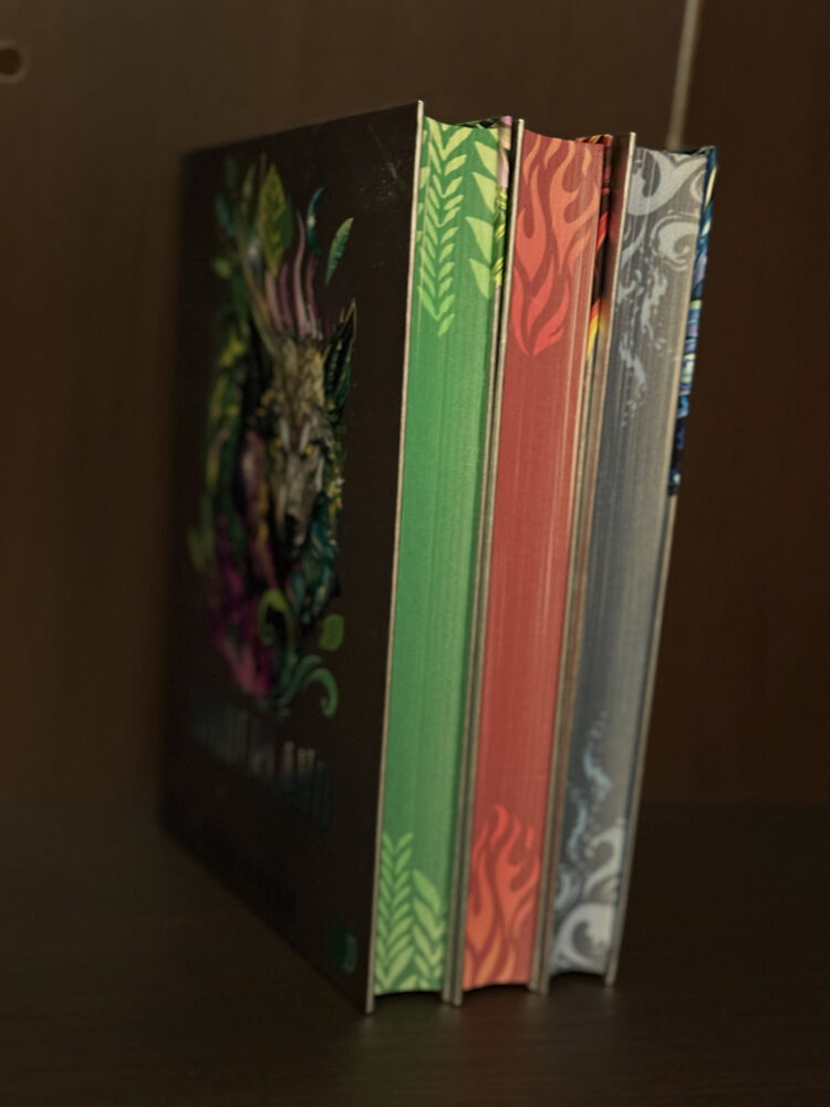 Drei B&auml;nde der Fantasy-Buchreihe Wilderland von Gina Mayer mit farbenpr&auml;chtigen Tierwesen auf den Buchcovern